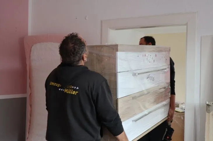 zwei umzugshelfer tragen verpackten schrank durch wohnung